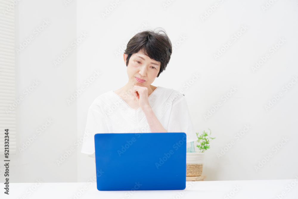 リビングでノートパソコンの前で考えるシニア女性