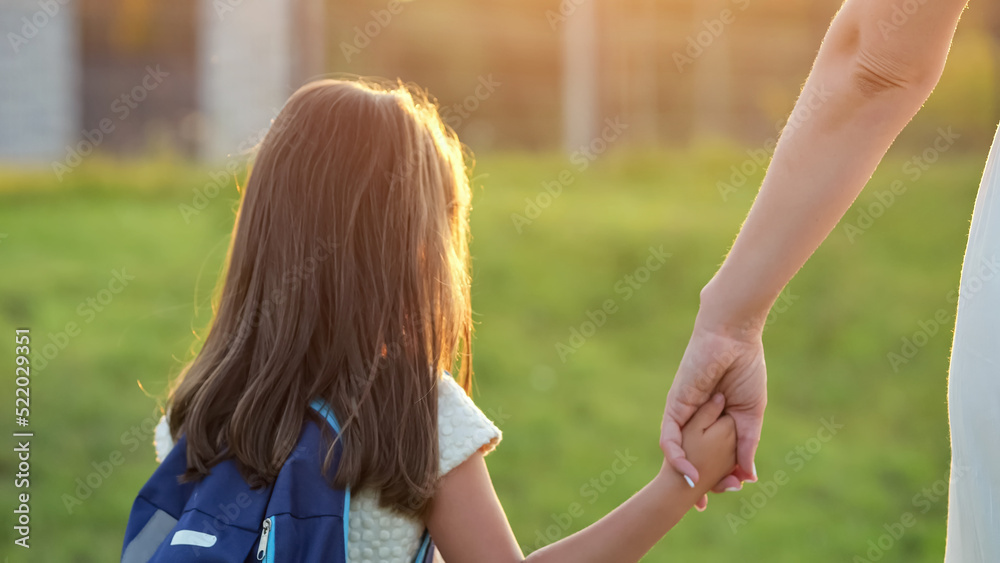 女学生放学后和妈妈一起回家。穿着蓝色双肩包和白色连衣裙的女孩抱着飞蛾