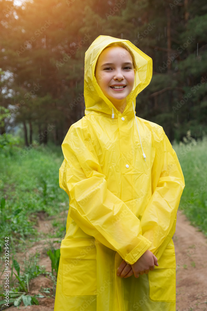 雨天，穿着黄色雨衣的快乐女孩站在森林里。青少年在森林里享受美丽的自然