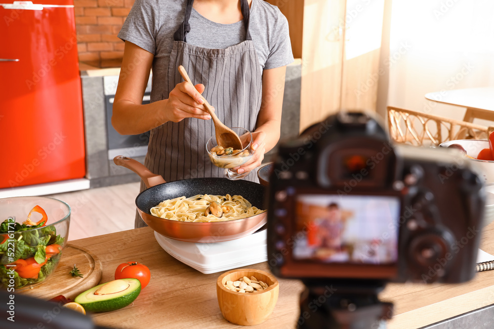 一名年轻女子在厨房录制烹饪视频课时在意大利面中加入贻贝