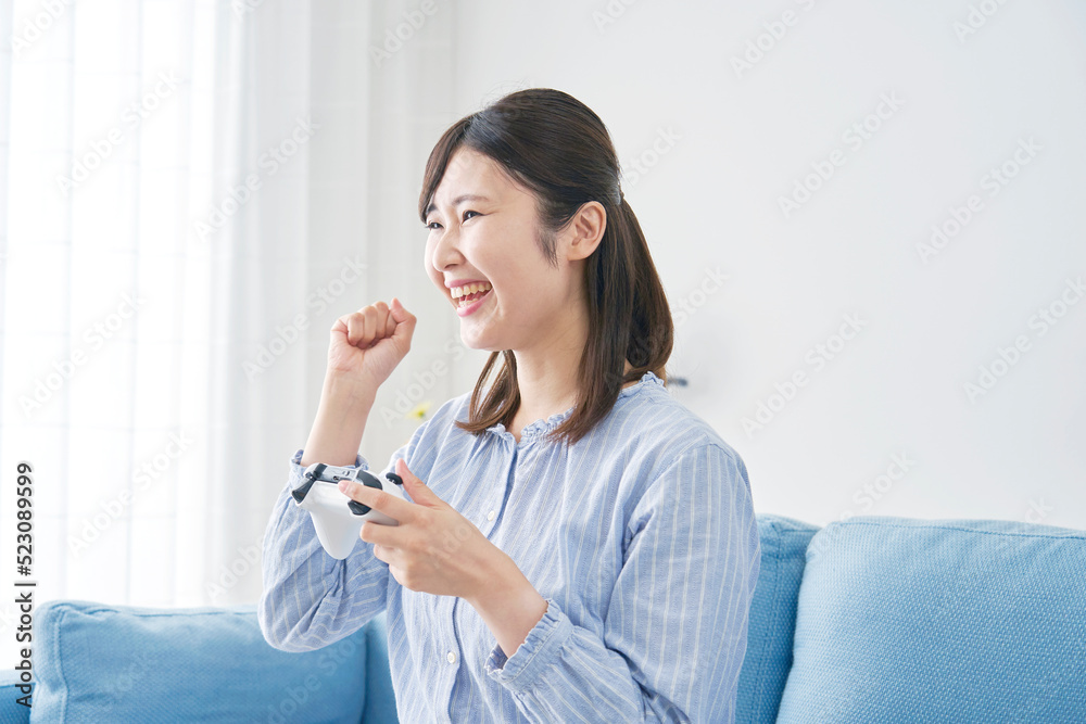自宅で一人でテレビゲームをしてガッツポーズをする女性