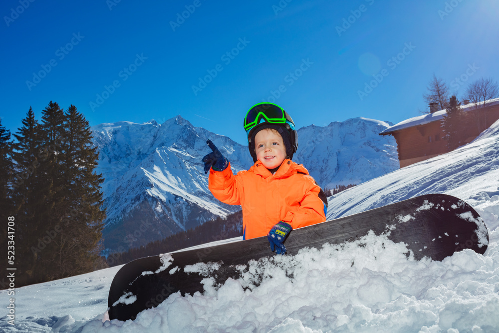 滑雪板男孩在高山滑雪道上指指点点，面带微笑