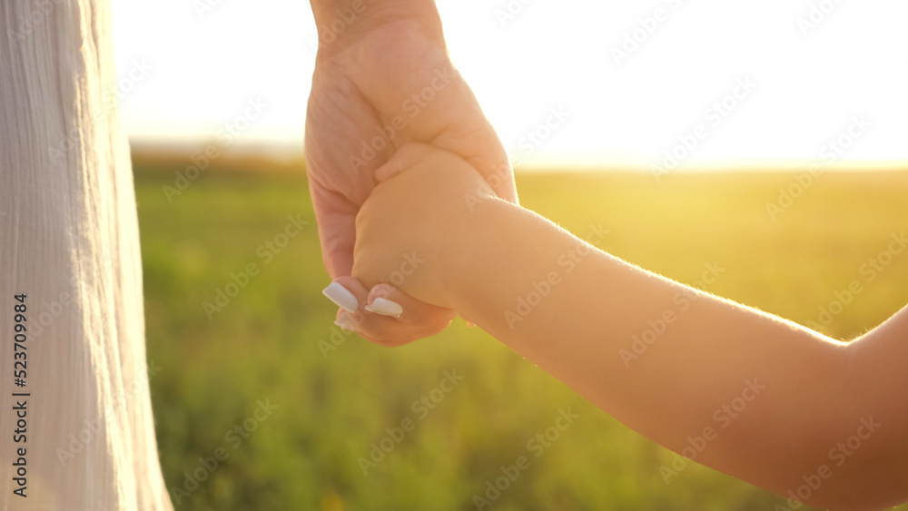 孩子牵着妈妈的手在绿色的草地上。父母和孩子站在一起向彼此展示纯真的爱