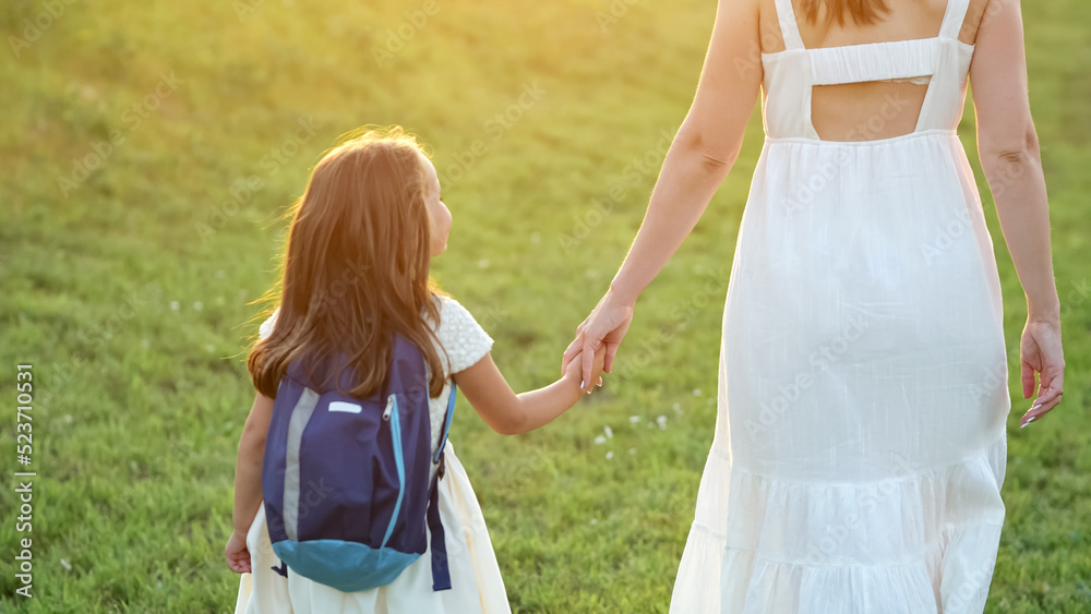 女学生放学后和妈妈一起回家。背蓝色背包、穿白色连衣裙的女孩抱着飞蛾