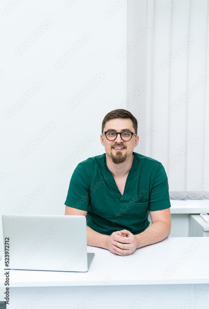 使用笔记本电脑的英俊医学专家。坐在电脑旁的专业年轻医生。