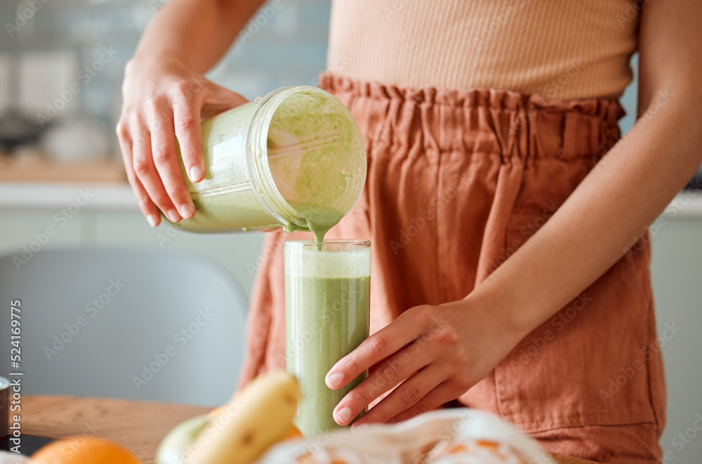 Woman pouring healthy smoothie in a glass from a blender jar on a counter for detox. Female making f