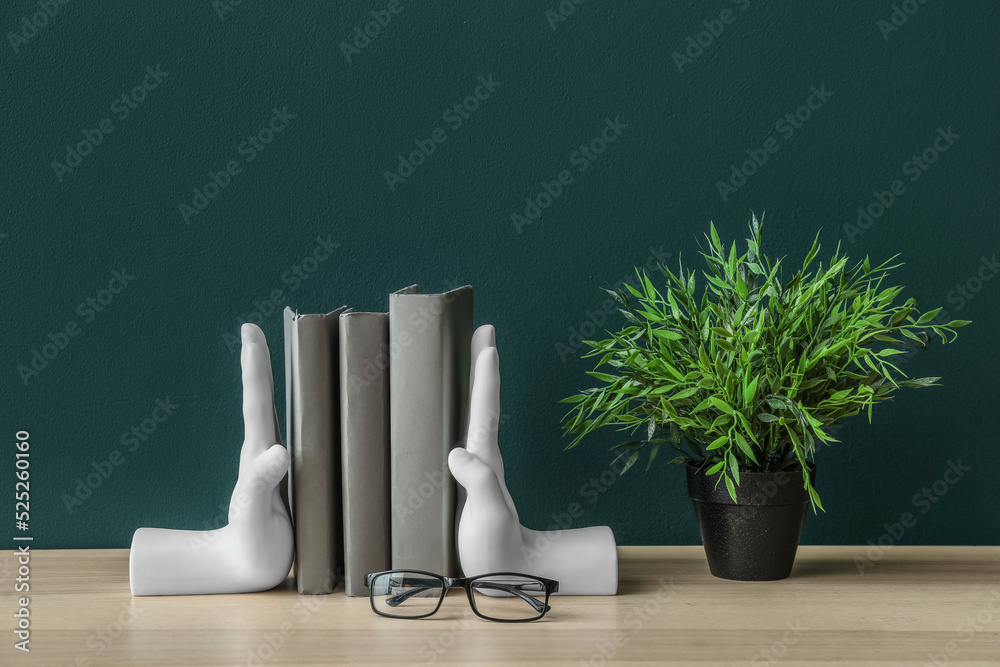 绿色墙壁附近的桌子上有时尚的支架，里面有书、眼镜和室内植物