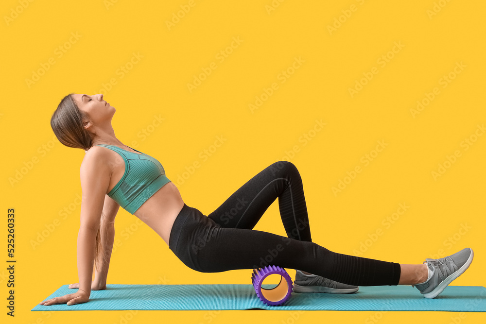 年轻女子用黄色背景的紫色泡沫滚轴锻炼