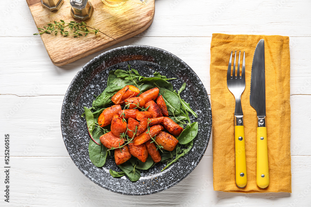 一盘美味的烤胡萝卜，配绿色蔬菜和浅色木质背景的餐具
