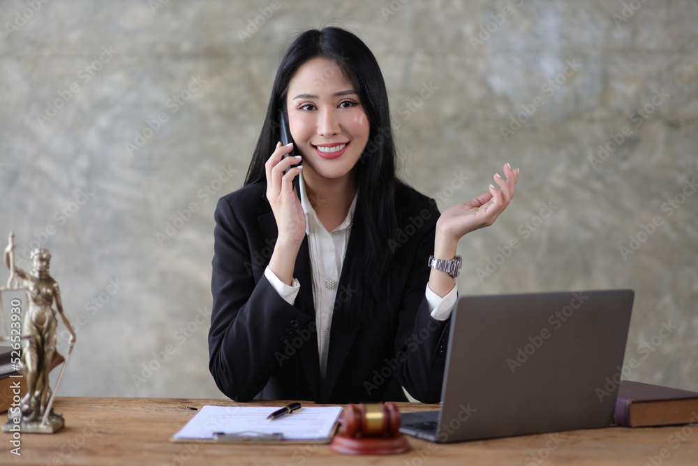 Female lawyer works on a laptop at a desk in a law firm while talking to a client on a mobile phone.