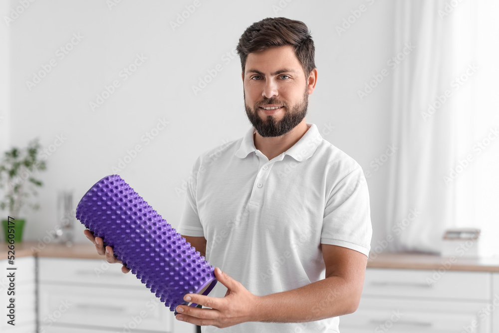 Young man with foam roller in kitchen