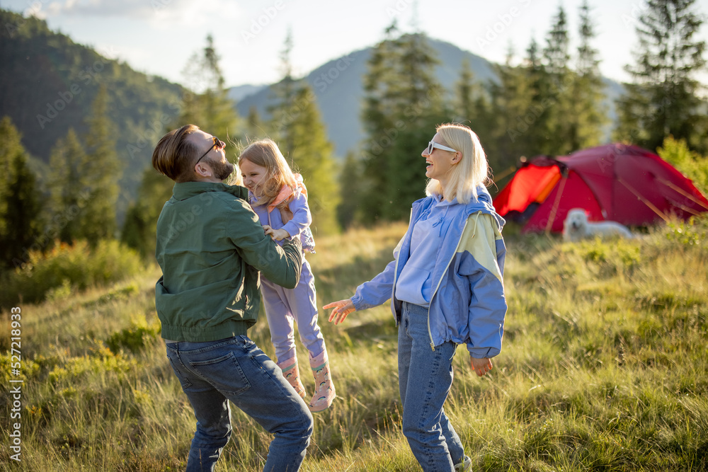 Young caucasian couple with little girl have fun while travel with tent in the mountains. Happy fami