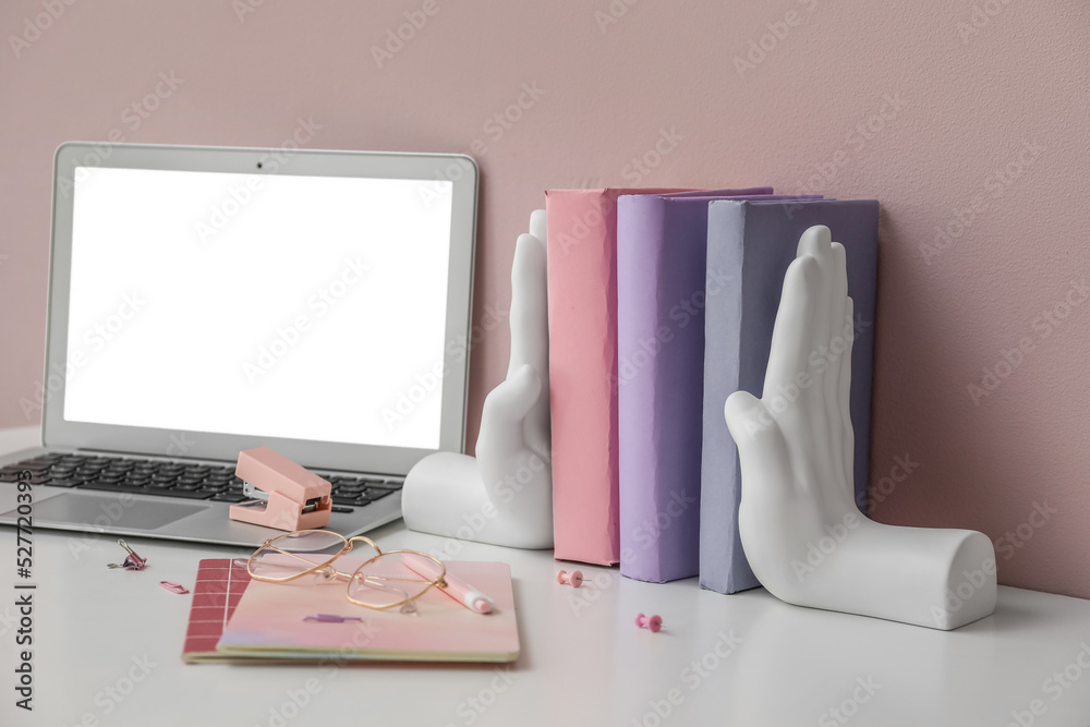 粉红色墙壁附近的桌子上放着时尚的支架，里面有书、笔记本电脑和眼镜
