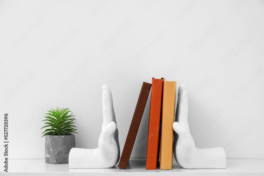 Stylish holder with books and flowerpot on table near grey wall