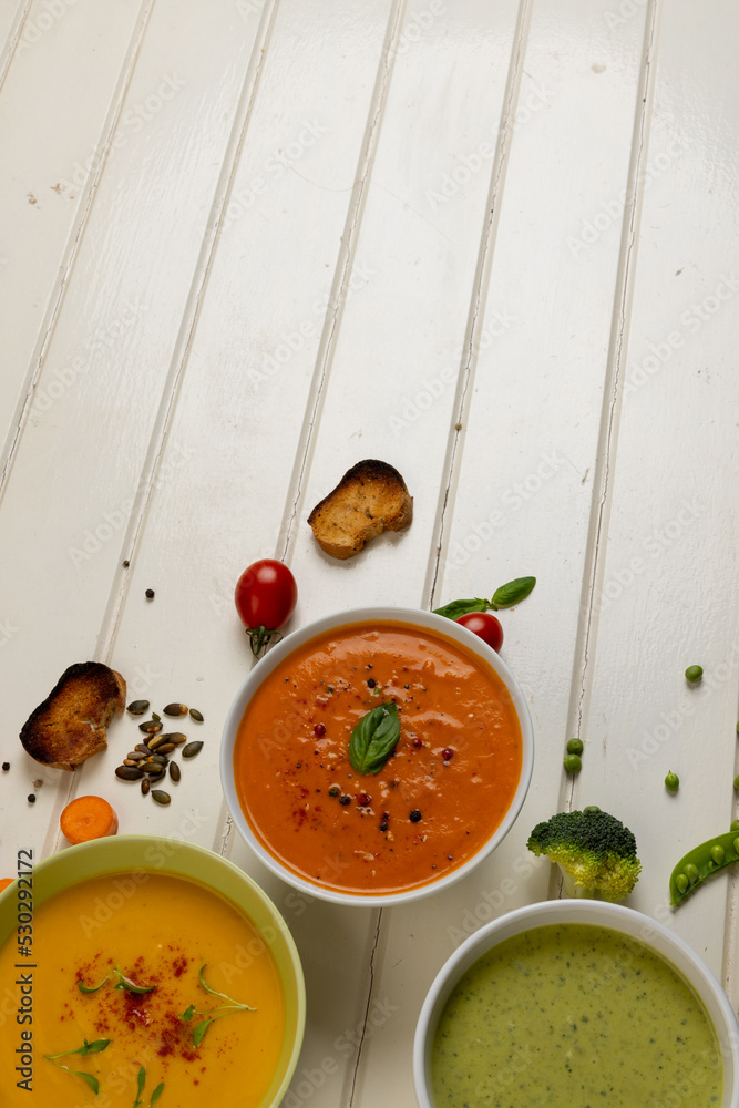 白木头上一碗碗胡萝卜、西兰花和番茄汤的垂直图像，复制空间