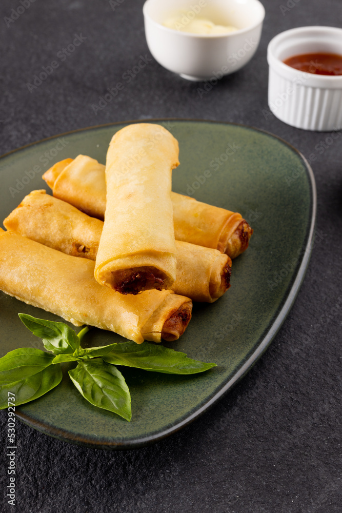 Close up of asian spring rolls on grey plate and condiments on grey background