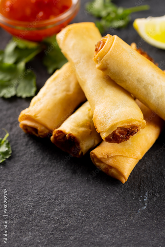 Close up of asian spring rolls, sliced lime and chilli sauce on grey background