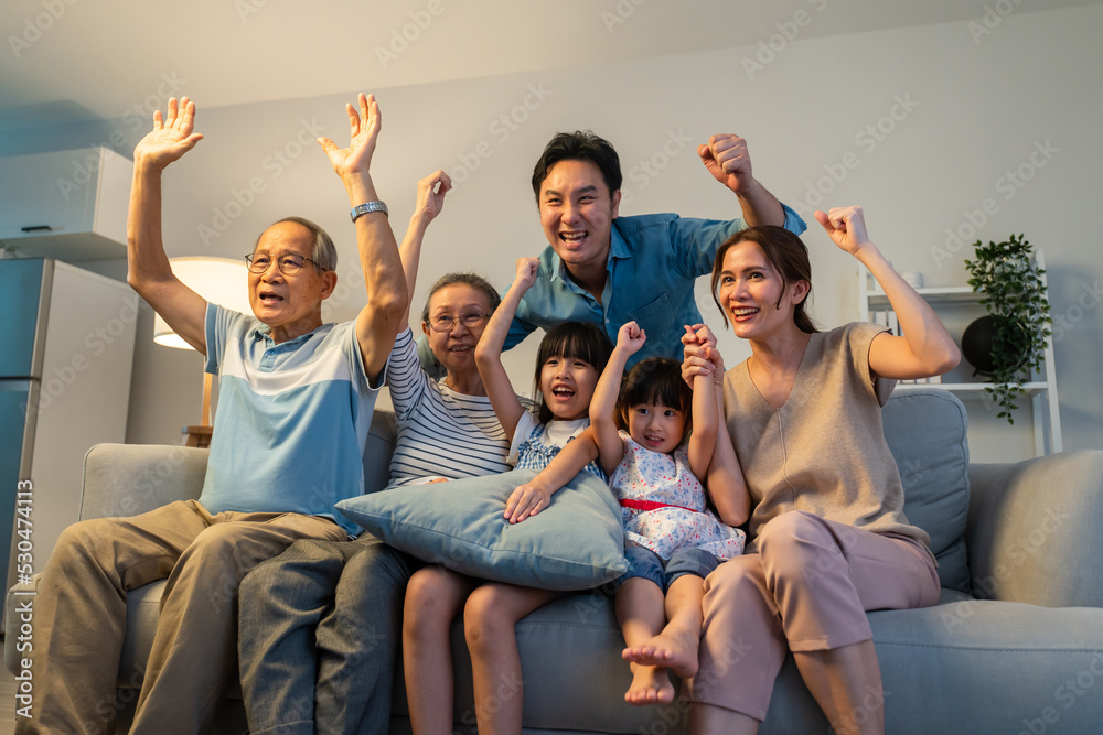 亚洲家庭在家里通过电视欢呼和观看足球比赛。