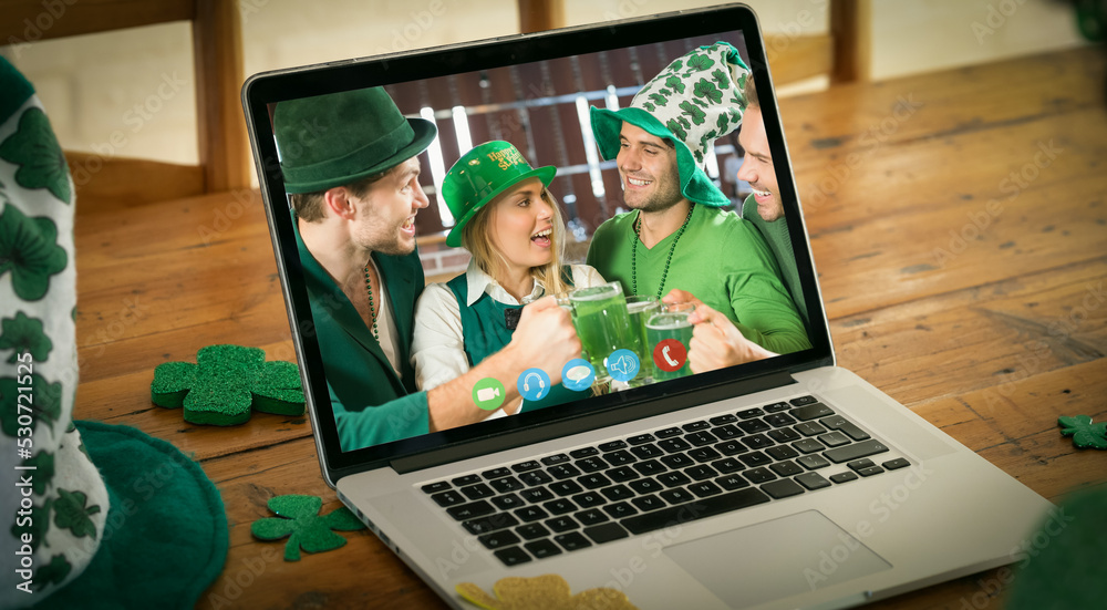 快乐的白人朋友戴着帽子在家里的笔记本电脑屏幕上进行圣帕特里克节视频通话