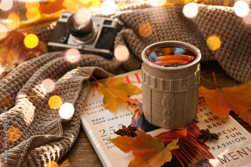 桌上有一杯美味的热葡萄酒、秋叶、格子和杂志
