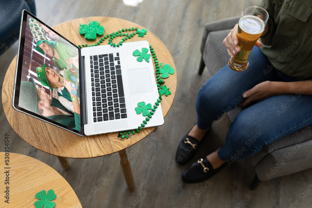 在酒吧用笔记本电脑进行视频会议时，一名妇女拿着啤酒杯的中段