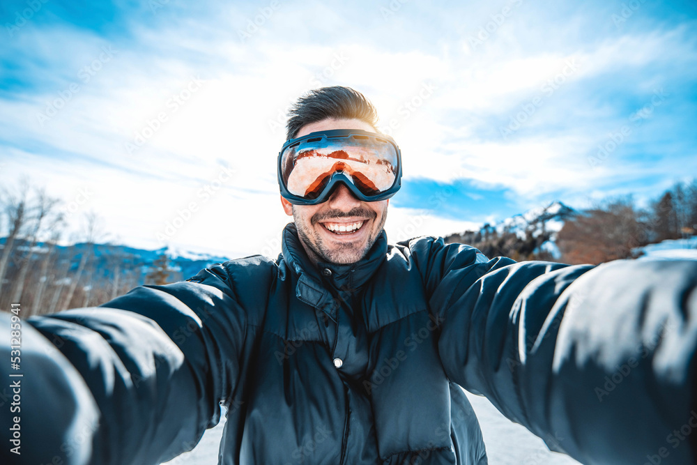 Young man taking selfie picture with smart cell phone hiking mountain on snowy slope - Happy skier h