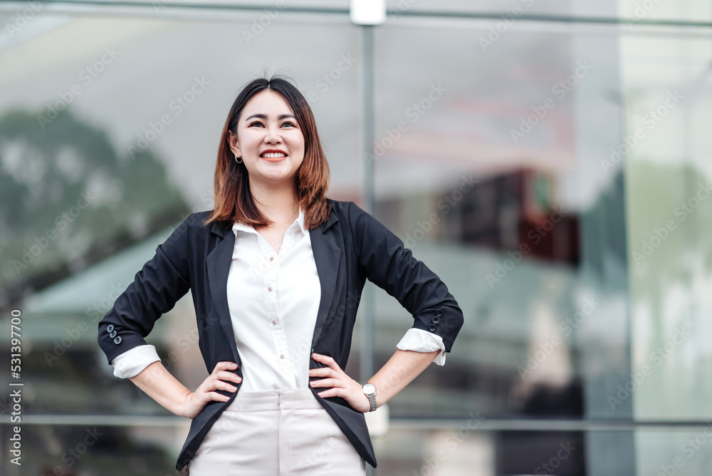 年轻的亚洲商务女性在机场航站楼外叉腰微笑的肖像