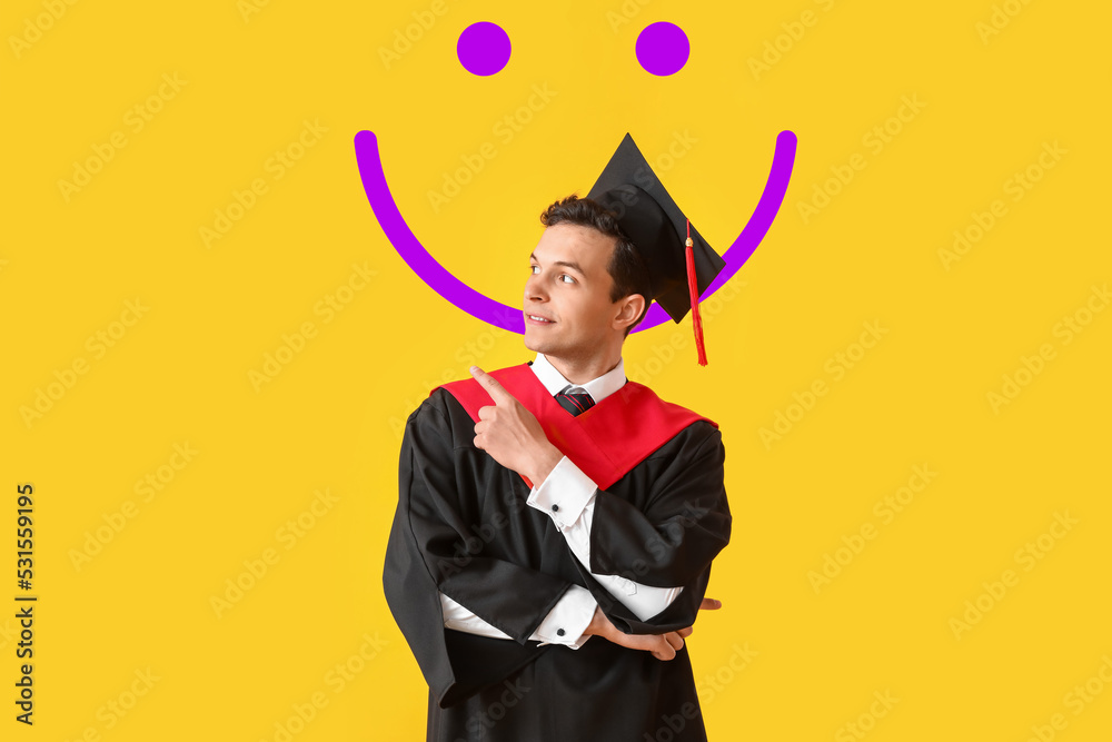Male graduating student pointing at something and drawn smile on yellow background