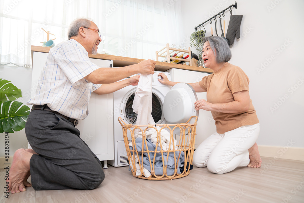 Senior couple working together to complete their household chores at the washing machine in a happy 