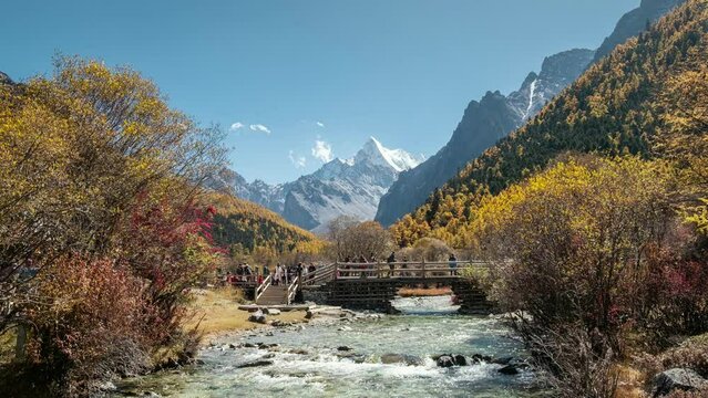 Holy mountain Chana Dorje in autumn forest with tourists walking on wooden bridge and river flowing at Yading nature reserve