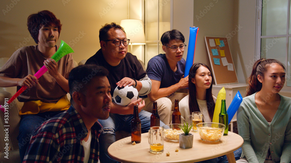 Happy Asian people with friends watching soccer or football on tv and celebrating victory at home, w