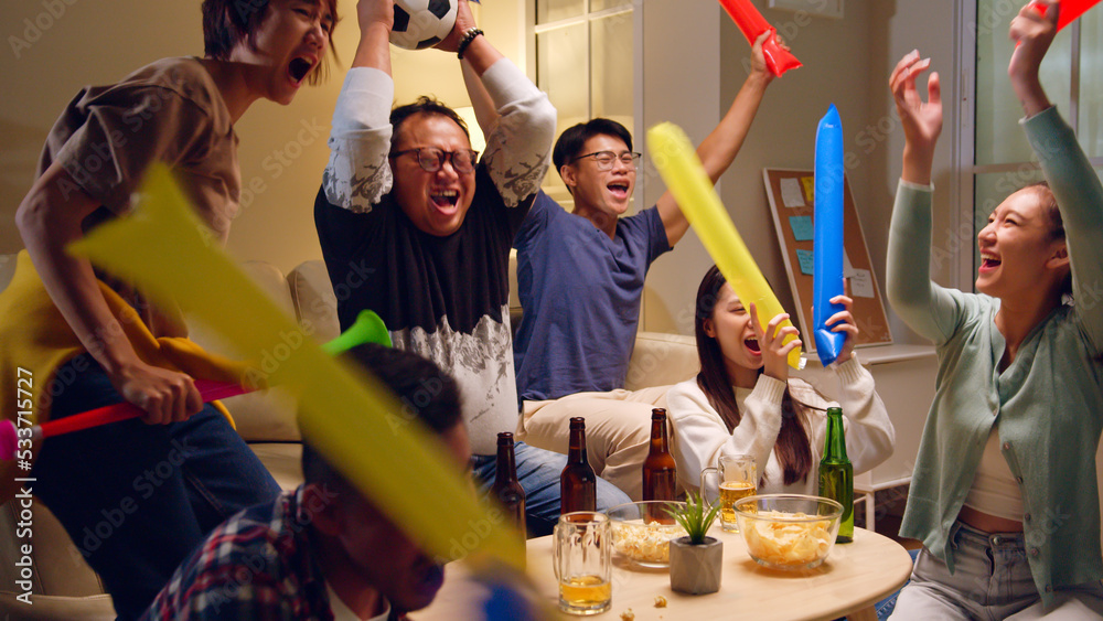 Happy Asian people with friends watching soccer or football on tv and celebrating victory at home, w