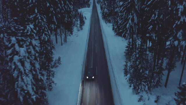 Aerial view of car driving on a mountain road in between spruce forest in a sunset. Frozen, cold and dark.