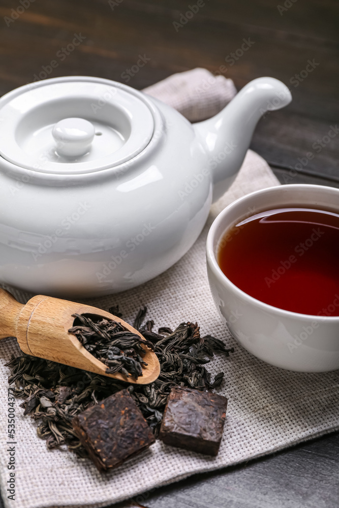 深色木质背景上的餐巾，配一勺干普洱茶、杯子和茶壶，特写