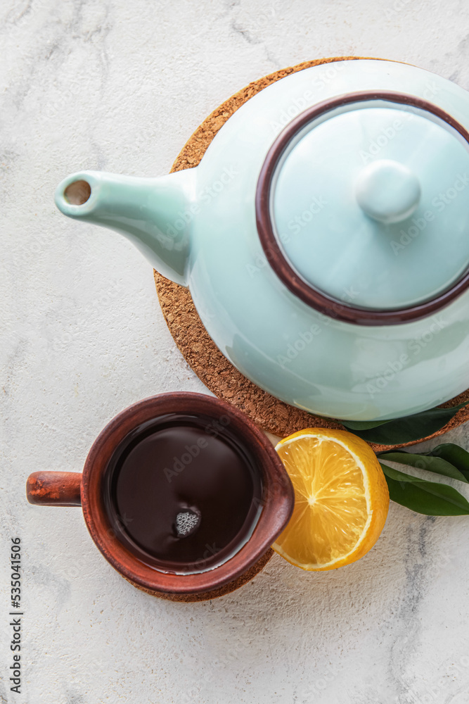Cup of black tea and teapot on light background, closeup
