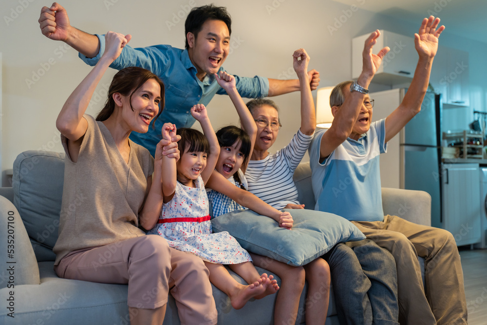 亚洲家庭在家里通过电视欢呼和观看足球比赛。