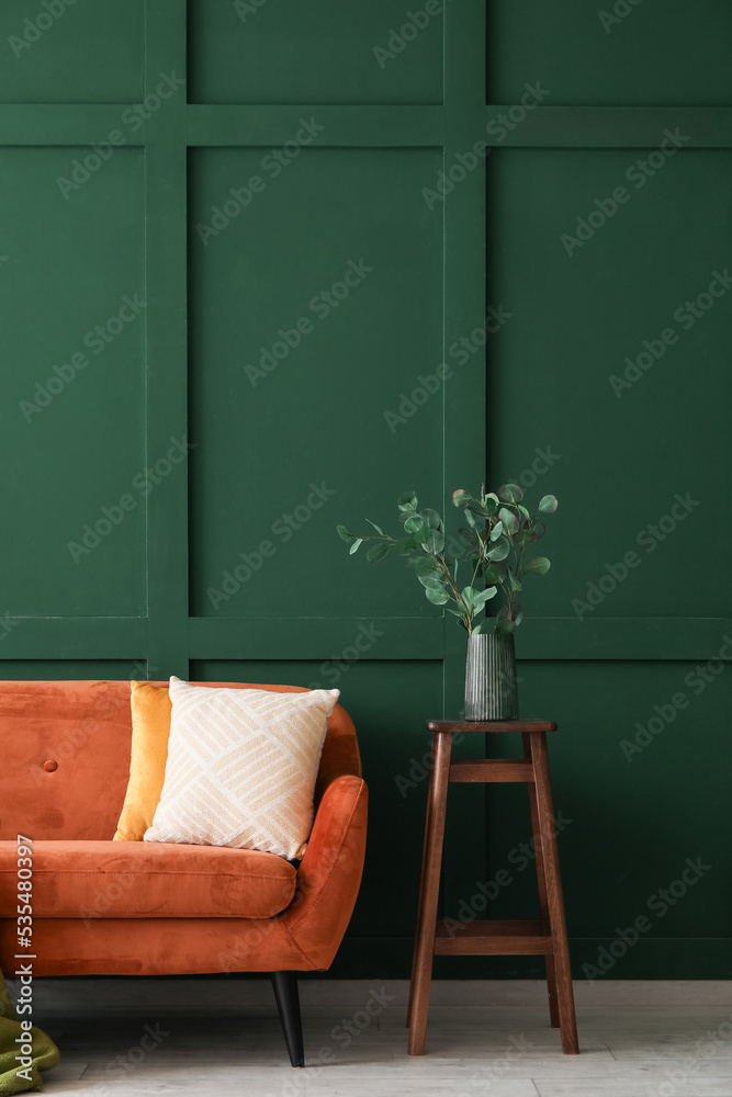 桌子上有桉树树枝的花瓶，靠近绿色墙壁的红色沙发