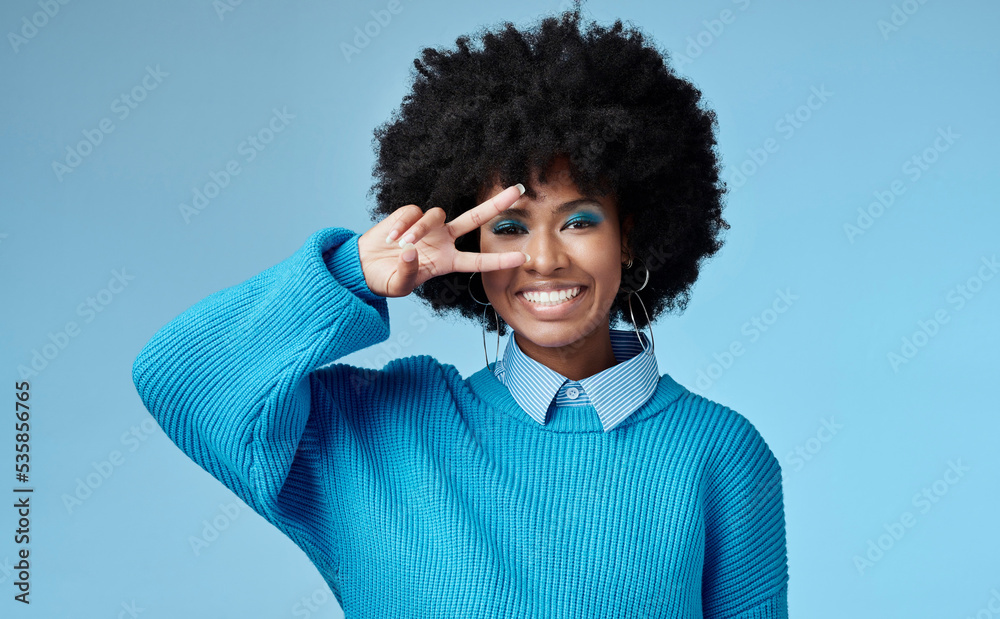 年轻的黑人女性，展示和平标志，蓝色工作室背景，时尚风格和非洲风格。微笑，h