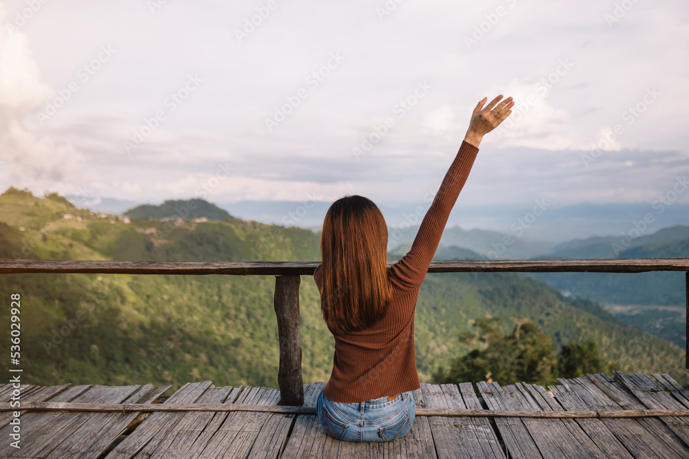 一位女性旅行者坐在那里眺望美丽的山脉、天空和自然的后视图像