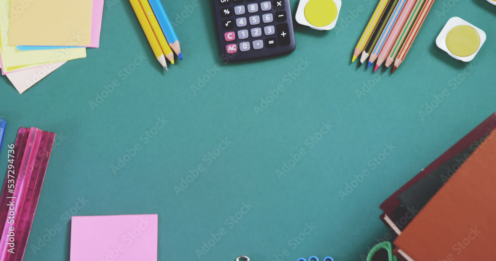 蓝色桌子上彩色铅笔、计算器、尺子、便签和书籍的俯视图