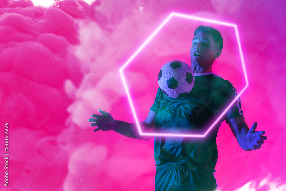 白人男性球员在粉红色霓虹灯烟雾下，在发光的六边形上玩足球