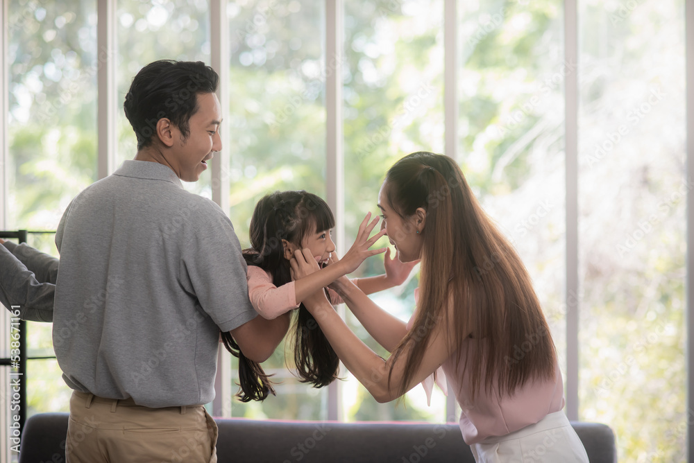 幸福的亚洲家庭，一个父亲抱着他的女儿，母亲站在他们两个身边，大笑