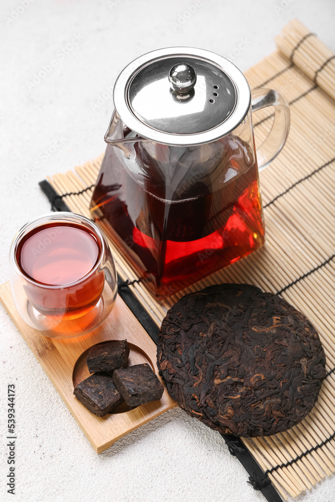 Board with dry pressed puer tea, glass and teapot on white background
