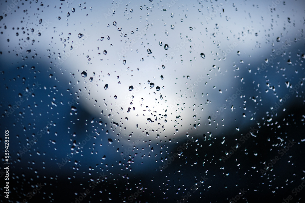 蓝色背景下窗户玻璃上的雨滴。选择性聚焦。雨天城市背景