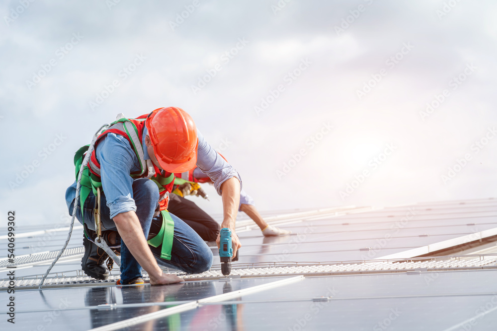 太阳能电池板技术人员带钻机在屋顶工厂安装太阳能电池板。