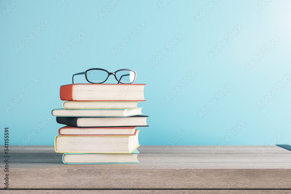 模糊蓝色背景上堆叠的书籍和眼镜的特写，带有模拟场所。学校和教育