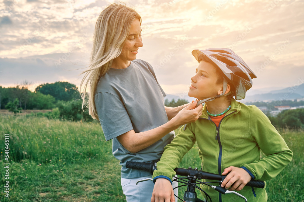 Mother teaching son to ride bicycle. Happy cute boy in helmet learn to riding a bike in park on gree