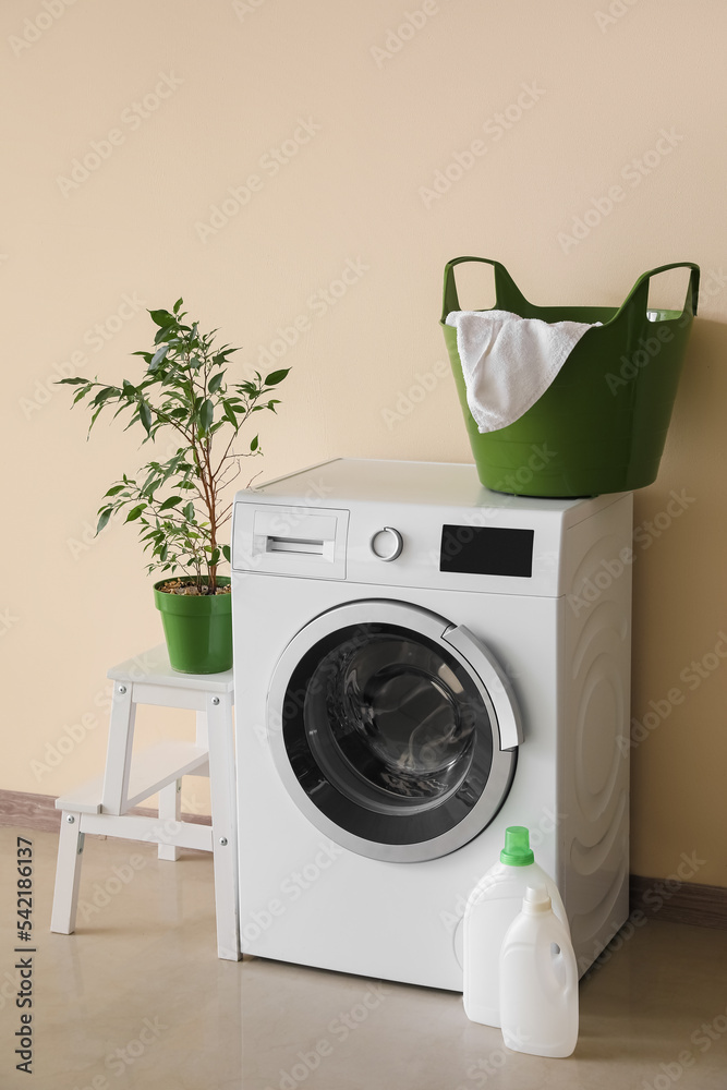 洗衣机，带洗衣篮，阶梯上的室内植物和米色墙壁附近的洗涤剂