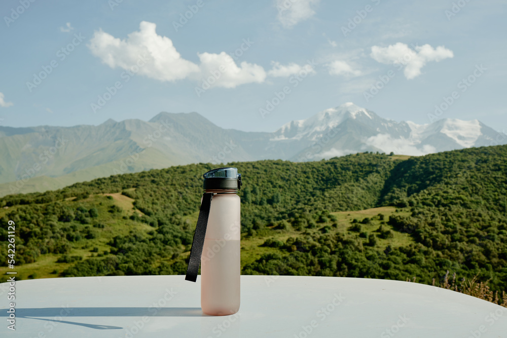 运动米色塑料水瓶，带表带，以山地自然为背景。概念o