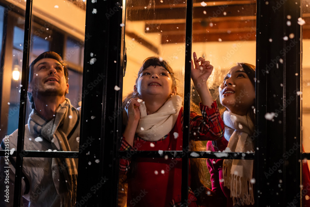 可爱的孩子看着窗户，和家人一起看第一片雪花。